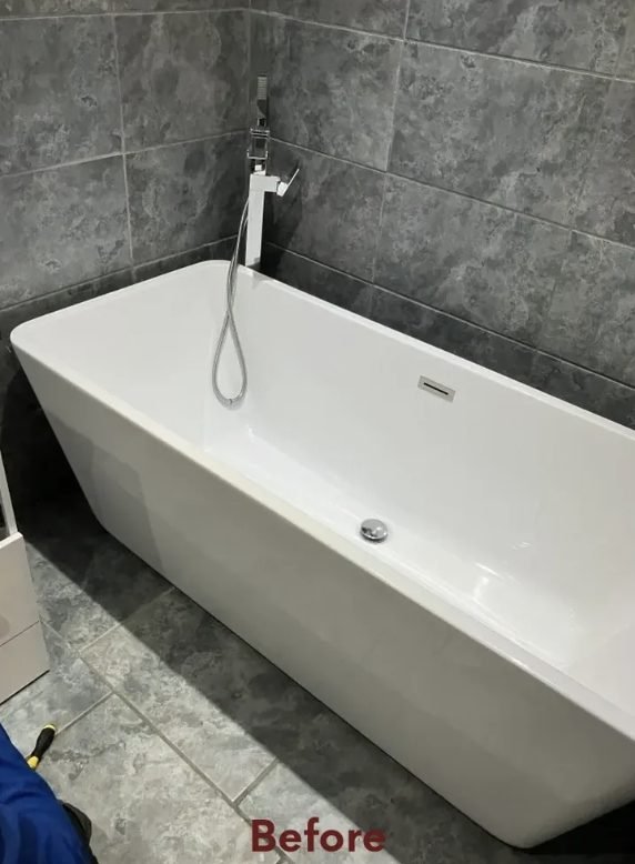 Bathroom before refit, freestanding bath against grey tiled wall